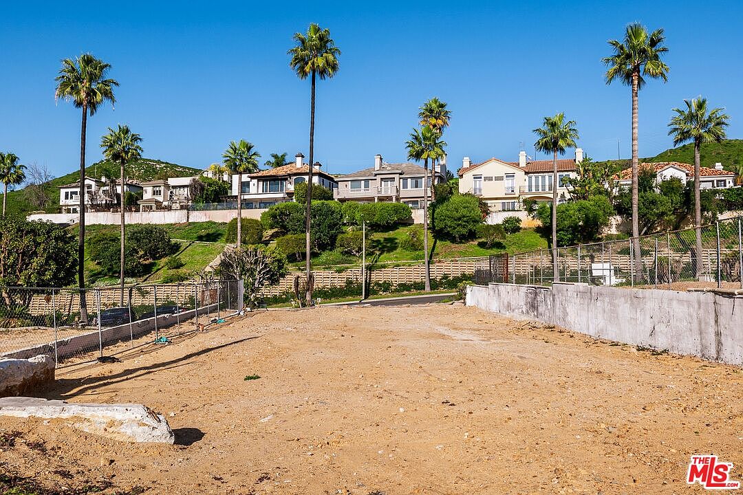 Cleared lot showing buildable pad with palm trees and homes beyond